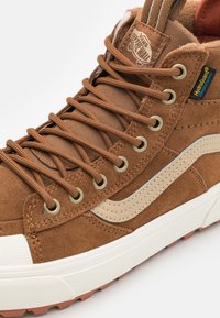 Brune semskede høje sneakers med beige sidebeklædning, metaløjer og strukturerede snørebånd. Har en gummisål i hvid-brun.