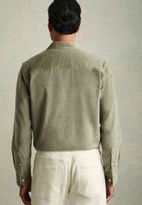 Cămașă din bumbac fâșie verde măslin cu mâneci lungi, cu manșete cu capse și un model de căptușeală, asociată cu pantaloni ușor bej. Material texturat.