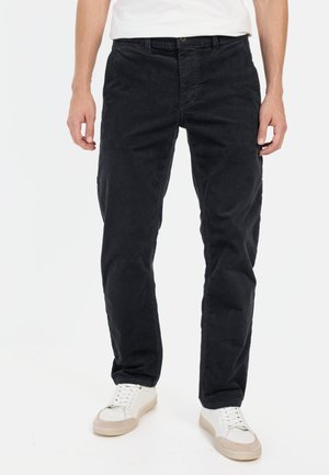 Zwarte corduroy broek met een rechte snit, voorzien van een ritssluiting, zijzakken en een subtiele textuur, gedragen met witte sneakers.