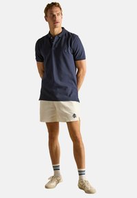 Tumed polo särgid lühikeste varrukatega, millele on lisatud heledatest beežidest šortse, millel on logo; kerge värvusega tennis jalanõud ja triibulised põlvesokid lõpetavad välimuse.