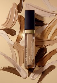 Estee Lauder Futurist concealer in een doorzichtig tubetje met een zwarte dop, omringd door kleurstalen van verschillende huidtinten in romige texturen.