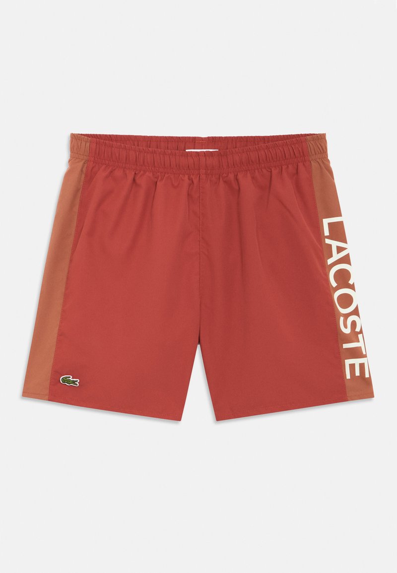 Calções de banho masculinos em vermelho com um painel lateral castanho. Apresentam um cós com cordão e o logótipo "LACOSTE" branco na lateral. Logótipo de crocodilo presente.