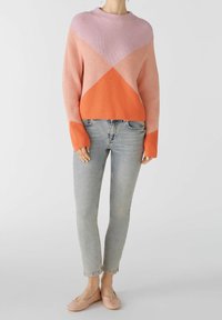 Gehaakte sweater in roze, lavendel en oranje met een ribbelstructuur; gecombineerd met lichtblauwe jeans en roze ballerina's.