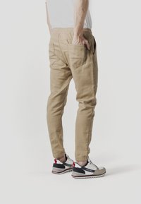 Pantalones de chándal caqui con cintura elástica y bolsillos laterales, con un corte relajado y detalles de costuras visibles. Combinados con zapatillas deportivas.