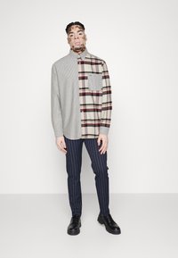 Hemd mit halber hellgrauer Rippstruktur und halber karierter Beigefarbe mit Burgunderrot. Ergänzt durch navy-gestreifte Hosen und schwarze Schuhe.