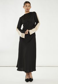 Vestito lungo nero a maniche lunghe con accenti in satin crema alle maniche. Tessuto liscio e fluido con una vestibilità comoda e un design minimalista.