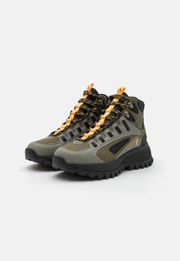Hiking boots in olive green and black with bright orange laces. Features high ankle support, textured rubber sole, and side accents.