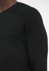 Čierny pletený sveter s žebrovanou textúrou na ramenách a hladkým telom, s klasickým okrúhlym výstrihom.