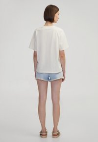 Crème oversized t-shirt met korte mouwen, van katoen, met een ronde halslijn, gecombineerd met lichtdenim shorts met een rafelrand en tan sandalen.