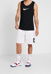 Černé tílko Nike s bílým logem, bílé kraťasy a bílé ponožky s černým logem. Boty v bílé barvě s červenými a modrými akcenty.