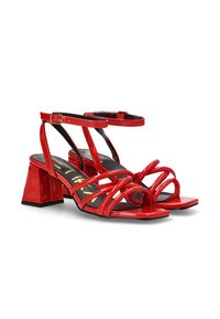 Sandalias de tacón de cuero sintético rojo con tacón cuadrado, que presentan múltiples tiras finas sobre los dedos y el tobillo. Plantilla negra con detalles dorados.