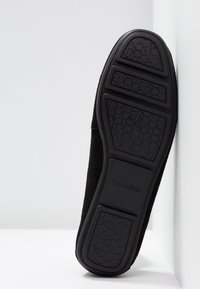 Semelle de chaussure en cuir suédé noir avec caoutchouc texturé pour une meilleure adhérence, logo embossé et motif distinct pour la durabilité.