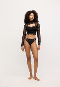 Svart långärmad topp i spets med blommönster och utskuren detalj, kombinerad med matchande spetsunderbyxor med sidoremmar och rosettaccent.