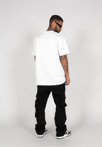 Hvid oversized t-shirt og sorte cargo bukser med flere lommer, båret med sorte solbriller og sort-hvide sneakers.