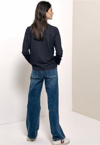 Navy textured sweater with long sleeves, paired with wide-leg blue denim jeans and white sneakers with red accents.