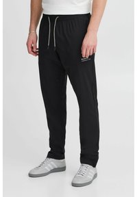 Pantalones jogger negros con cintura elástica y cordón, con bolsillos laterales y detalle de logo. Combinados con zapatillas grises.
