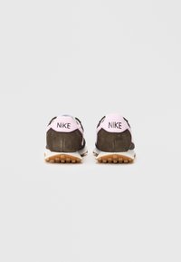 Nike čevlji z zgornjim delom iz rjave nubuk usnja, roza ovratnikom na peti in črnimi mrežastimi deli. Vsebujejo belo srednje podplate in teksturirano gumijasto podplate.