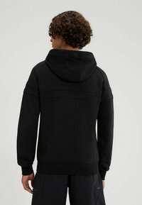 Sudadera negra con capucha ajustable, puños y dobladillo acanalados. Textura suave con diseño minimalista y sin patrones visibles.