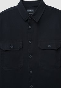 Camicia in denim nero con colletto classico, due tasche sul petto, chiusura con bottoni e tessuto testurizzato. Presenta bottoni e cuciture scuri coordinati.
