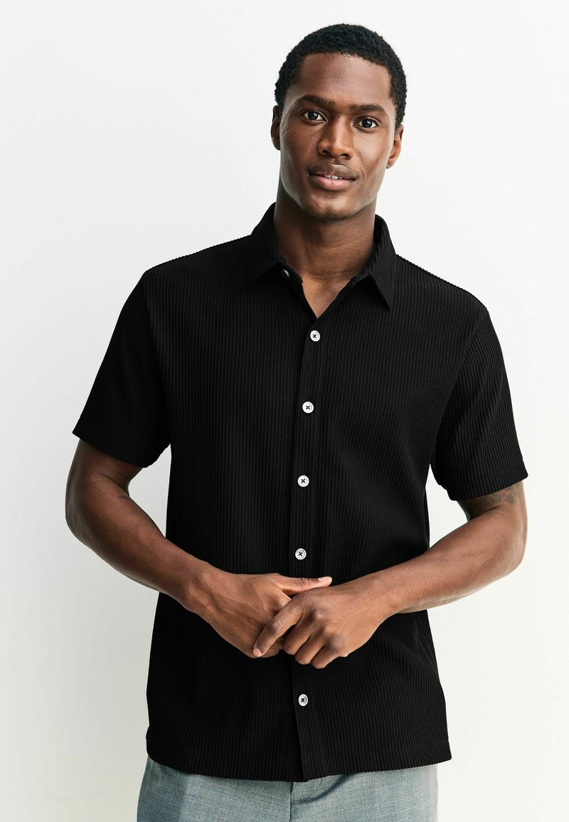 Schwarzes Kurzarmhemd mit geripptem Textil, tailliertem Design und weißen Knöpfen. Glattes Material und klassischer Kragen.