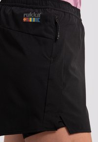 Shorts sportivi neri con cintura elastica, tasca laterale e texture perforata. Presentano un logo sul davanti e fessure laterali per la mobilità.