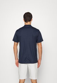 Marinblå kortärmad polo med ståkrage, tillverkad av slät tyg, med rak nederkant och axelsömmar för en atletisk passform.