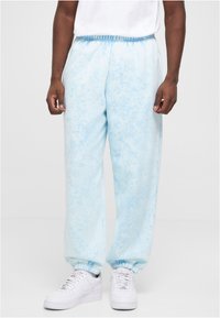 Lyseblå tie-dye joggebukser med elastisk liv og mansjetter, laget av mykt stoff. Kombinert med hvite joggesko for kontrast.
