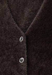 Brun fluffig cardigan med V-halsdesign. Har släta knappar i silver med ingraverad text. Mjuk textur och shaggy utseende.