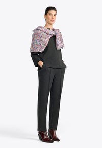 Donkergrijs, textuurig topje gelaagd onder een meerkleurige gebreide omslagdoek. Bijpassende tapered grijze broek en bordeauxrode enkellaarsjes met hak maken de outfit compleet.