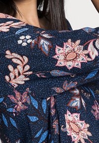 Chemise marine ornée d'un motif floral dans des teintes de rose, bleu et marron, en tissu à texture lâche et avec un design encolure en V.