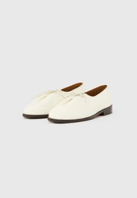 Chaussures en cuir blanc avec une surface texturée, un bout arrondi et un talon plat marron. Elles disposent d'une fermeture à lacets et d'un design minimaliste.