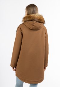 Bruine parka jas met een nepveren capuchon, lange mouwen en een iets langere achterkant. Bevat naaddetails en een gladde textuur.