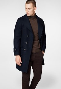 Granatowy płaszcz dwurzędowy z wełny, z dużymi klapami, metalowymi guzikami i dopasowanym krojem. Noszony na brązowym golfie.