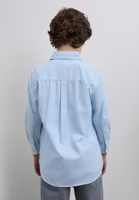 Ljusblå skjorta med lång ärm, knappkrage, veck på ryggen och knappade manschetter. Mjukt tyg med en avslappnad passform.