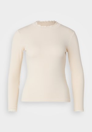 Langermet, ribbestrikket topp i off-white med volanger i høy hals og mansjetter. Glatt tekstur med en figurnær silhuett.