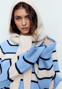Maglione a righe azzurro chiaro e crema con cappuccio, caratterizzato da polsini a coste e una texture morbida. Notabile per le strisce nere orizzontali.