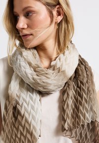 Écharpe légère et texturée présentant un dégradé de crème clair à marron avec un motif en diamant. Tissu doux qui tombe librement autour du cou.