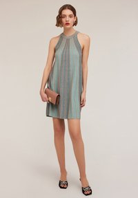 Vestido de punto con un cuello alto, que presenta rayas verticales en tonos turquesa y melocotón. Combinado con un bolso metálico y zapatos negros con lazos.