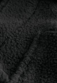 Detailný záber na jemnú čiernu fleecovú tkaninu s textúrovaným, chlpatým povrchom a viditeľnými záhybmi.