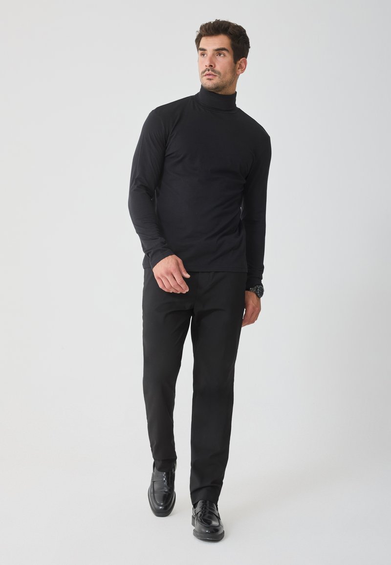 Cămașă neagră cu mâneci lungi și guler înalt, asortată cu pantaloni negri, completată de pantofi negri strălucitori. Textură netedă, design ajustat.