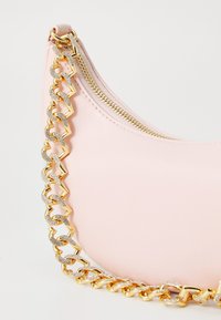 Rózsaszín bőr kézitáska ívelt dizájnnal, arany lánc fogantyúval és cipzárral. A lánc texturált és sima láncszemeket is tartalmaz.