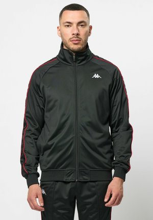Zwarte sportieve jack met rode zijstrepen, hoge kraag en rits aan de voorkant. Gemaakt van gladde stof, met logo op de borst en geribbelde manchetten.