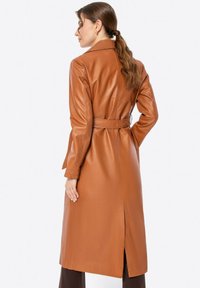 Brauner Leder-Trenchcoat mit taillierter Taille, langen Ärmeln und einem Schlitz hinten, der eine glatte Textur und einen maßgeschneiderten Schnitt aufweist.