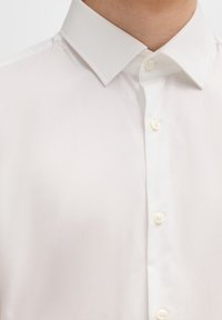 Witte button-up shirt met een gestructureerde kraag, een gladde textuur en vier ronde knopen langs de sluiting. Eenvoudig en minimalistisch ontwerp.