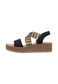 Black suede wedge sandals with patterned fabric straps featuring geometric designs in blue, gold, and red, and a woven jute midsole.