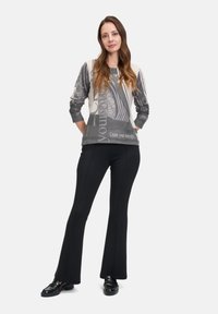 Grauer Pullover mit abstrakten Mustern und Text, kombiniert mit schwarzen Schlaghosen. Das Outfit zeichnet sich durch eine lockere Passform und weichen Stoff aus.