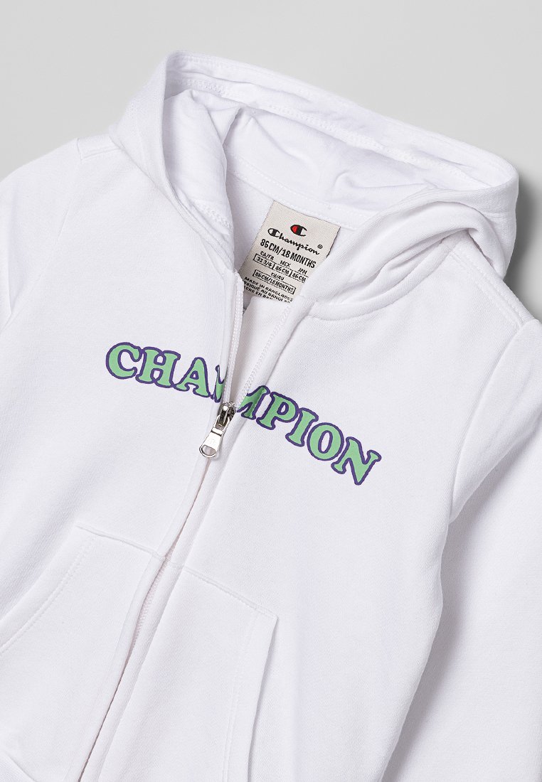 Felpa con zip bianca per bambino con cappuccio, tasche frontali e testo "CHAMPION" in viola contornato di verde sul petto.