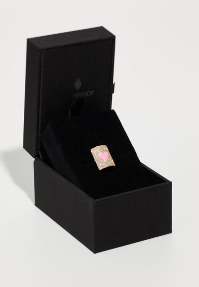 Anillo dorado con un diseño de corazón rosa sobre un fondo de purpurina dorada. Presentado en una caja de joyería cuadrada negra con un interior de suave terciopelo.