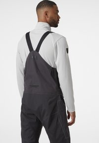 Pantalones de tirantes en negro y gris con tirantes ajustables, detalles de bolsillos y un diseño entallado, fabricados con un material texturizado y duradero.