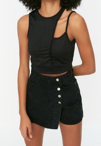 Černý zkrácený top s asymetrickým designem ramene, spojený s černou denimovou sukní s vysokým pasem, která má zapínání na knoflíky a boční kapsy.